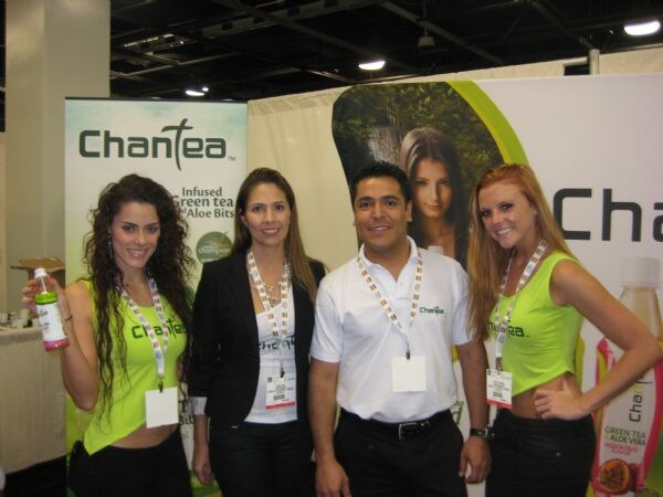 Two women in green tops, a woman in a black blazer and a man in a white shirt stand together at the ChanTea booth; one woman holds a bottle of ChanTea green tea.