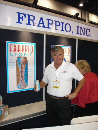 A man in a white polo with a badge holds a can of Frappio Light beside a Frappio Light poster under a Frappio, Inc. sign, with a woman in red behind him.
