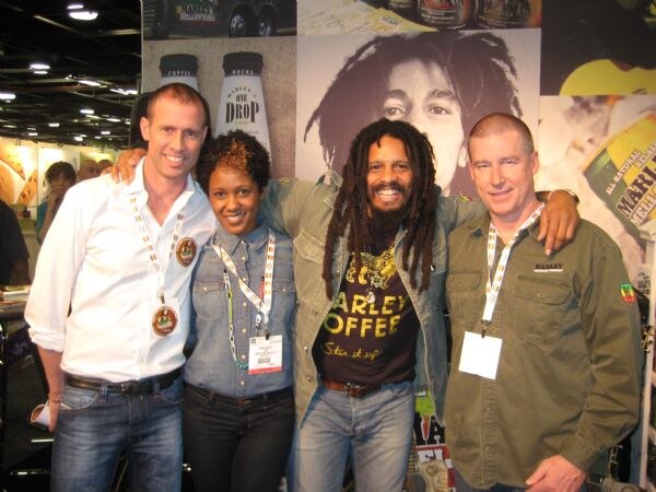 Four people with lanyards pose together in front of Marley Coffee and Marley's Mellow Mood displays, one wearing a Marley Coffee shirt.