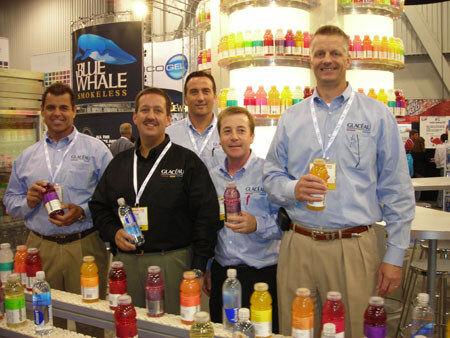 Four men in Glacéau shirts and lanyards hold bottled drinks in front of shelves of colorful bottles, with Blue Whale Smokeless and Cogel signs behind them.