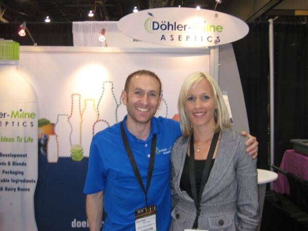 A smiling man in a blue Döhler-Milne polo and a smiling blonde woman in a gray blazer pose under an oval Döhler-Milne Aseptics sign.