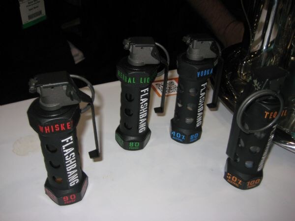 Four black grenade-shaped Flashbang bottles on a white table, labeled whiskey, herbal liqueur, vodka and tequila, each showing its proof.