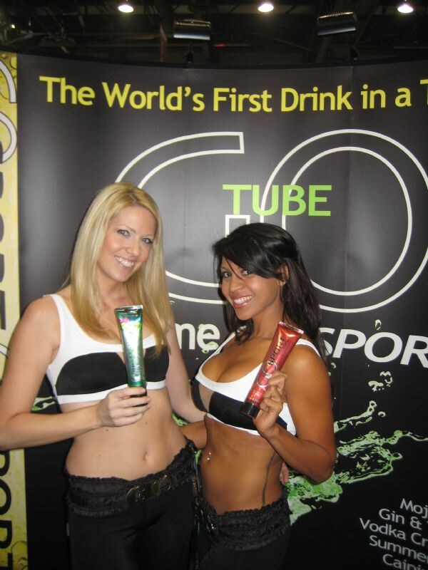 Two women in white and black tops hold Go Tube drink tubes, one green and one red, in front of a black Go Tube backdrop reading The World's First Drink in a Tube.