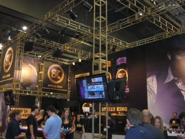 Wide view of the Street King booth with overhead truss lighting, SK logo banners, a video screen and attendees standing near the counters.
