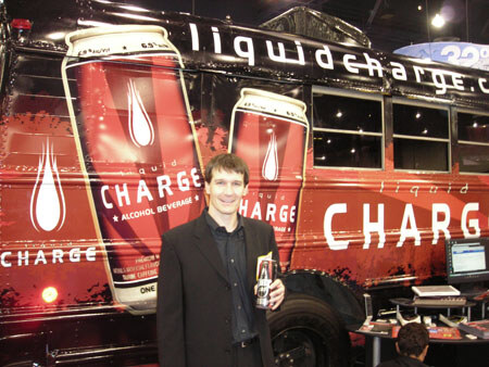 A man in a dark jacket holds a can in front of a bus wrapped with Liquid Charge alcohol beverage can graphics.