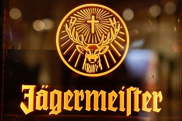 An illuminated orange Jägermeister sign showing a stag's head with a cross between its antlers inside a circle, with the brand name in gothic lettering below.