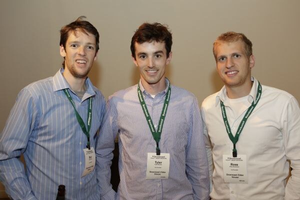 Three men in dress shirts and green lanyards stand side by side smiling. Tyler of Downeast Cider House is in the center and Ross of Downeast Cider House is on the right.