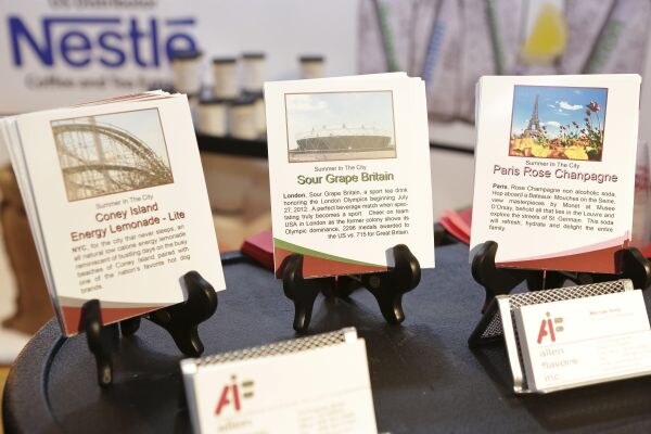 Three printed cards on small stands show concept beverages Coney Island Energy Lemonade - Lite, Sour Grape Britain and Paris Rose Champagne, with Allen Flavors business cards and a Nestle sign behind.