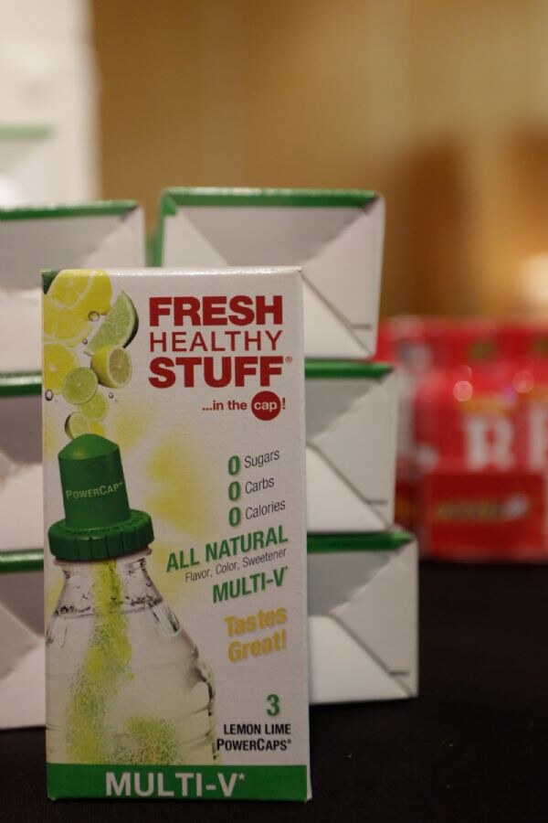 Box of Fresh Healthy Stuff Multi-V Lemon Lime PowerCaps in front of stacked white boxes with green trim, with a red package blurred behind.