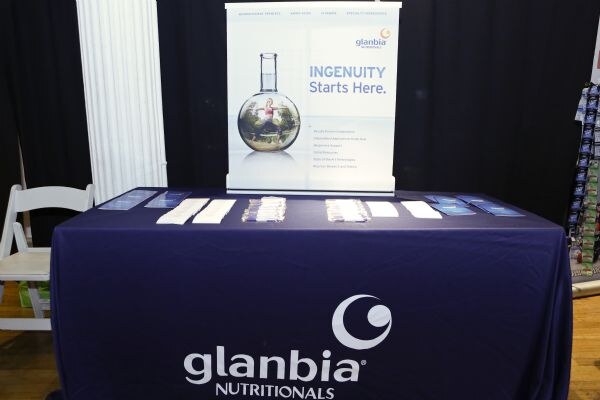 A navy table cloth with the Glanbia Nutritionals logo, with brochures and pens on top. A banner behind reads "Ingenuity Starts Here."