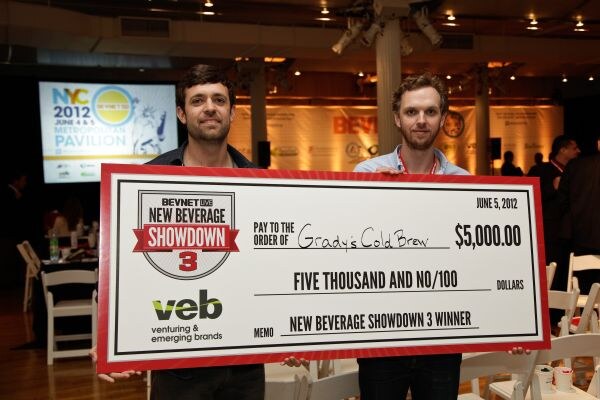 Two men hold a large check for $5,000 made out to Grady's Cold Brew, labeled New Beverage Showdown 3 Winner and bearing the VEB logo, in an event hall.