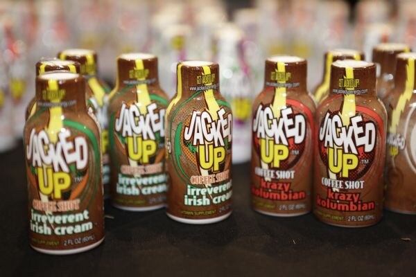 Rows of small brown Jacked Up coffee shot bottles in Irreverent Irish Cream and Krazy Kolumbian flavors standing on a dark table.