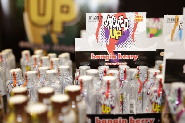 A Jacked Up Bangin Berry energy bomb shot display with rows of small white bottles, with more bottles and a blurred sign in the background.
