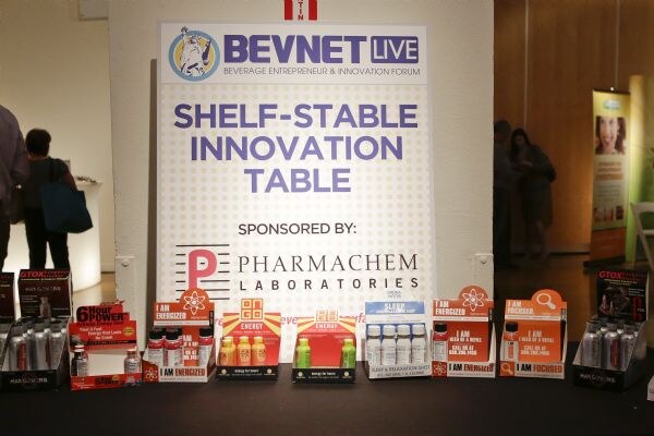 A BevNET Live sign reading Shelf-Stable Innovation Table, sponsored by Pharmachem Laboratories, above a table of energy shot displays including 6 Hour Power and I Am Energized.