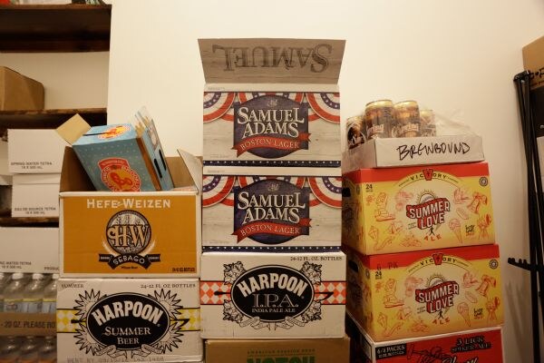 Stacked cases of beer: Samuel Adams Boston Lager, Harpoon IPA and Summer Beer, Sebago Hefe-Weizen, and Victory Summer Love, with a case marked Brewbound on top at right.