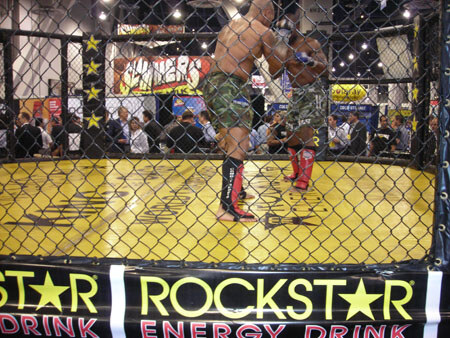 Two fighters in shorts square off inside a chain-link cage with a yellow floor, with Rockstar Energy Drink banners on the front and a Slammers sign and spectators behind.