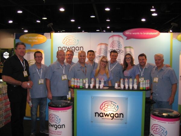 Ten people in matching blue shirts and lanyards stand in a row behind a counter at the Nawgan booth, with cans and cups on top and Nawgan logos on the display and barrels.