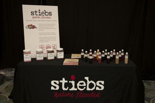 A black-draped stiebs table, labeled Nature Elevated, holds four jars and rows of small bottles in various colors, with a stiebs sign standing behind them.