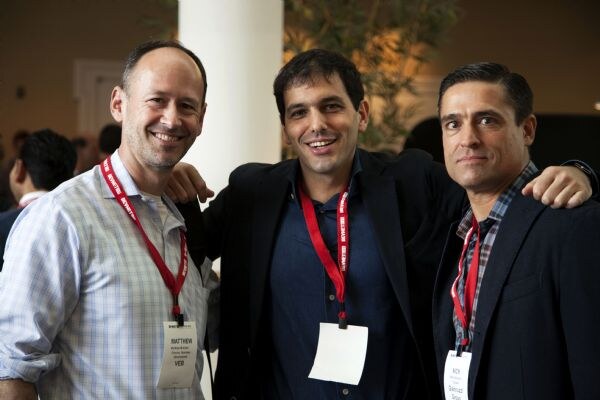 Three smiling men with arms around each other and red lanyards pose together; the man on the left wears a badge reading Matthew.