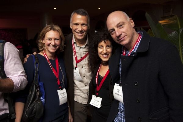Four smiling attendees in red lanyards pose close together. Amanda stands at the left, and Bill, a bald man in a dark jacket, stands at the right.