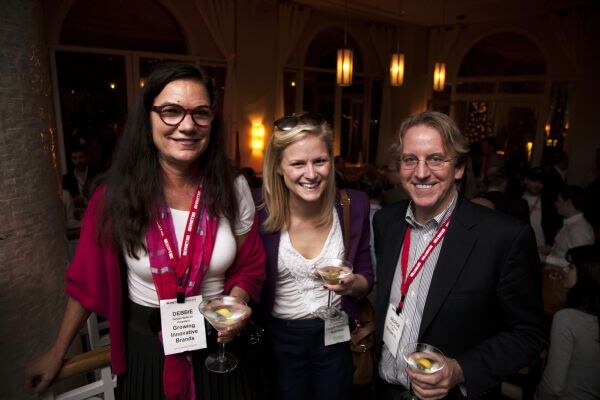 Debbie of Growing Innovative Brands, on the left, wears a pink scarf and glasses. She poses with a blonde woman and a man in glasses, who all hold martini glasses.