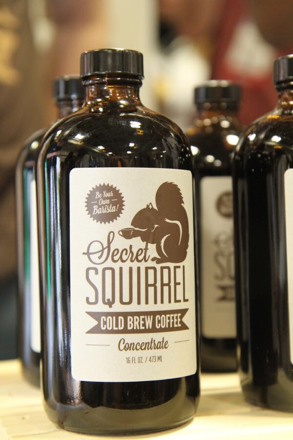 Close-up of dark glass bottles of Secret Squirrel Cold Brew Coffee Concentrate, 16 fl oz, with a label showing a squirrel holding a cup and the phrase Be Your Own Barista.