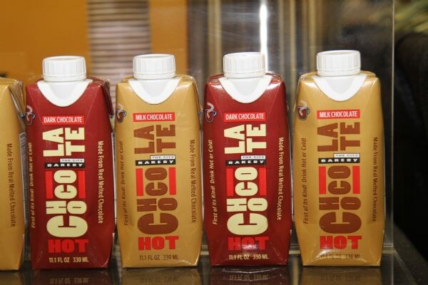 Four cartons of The City Bakery hot chocolate stand in a row: two dark chocolate in red and two milk chocolate in tan, each labeled Chocolate Hot, 11.1 fl oz.
