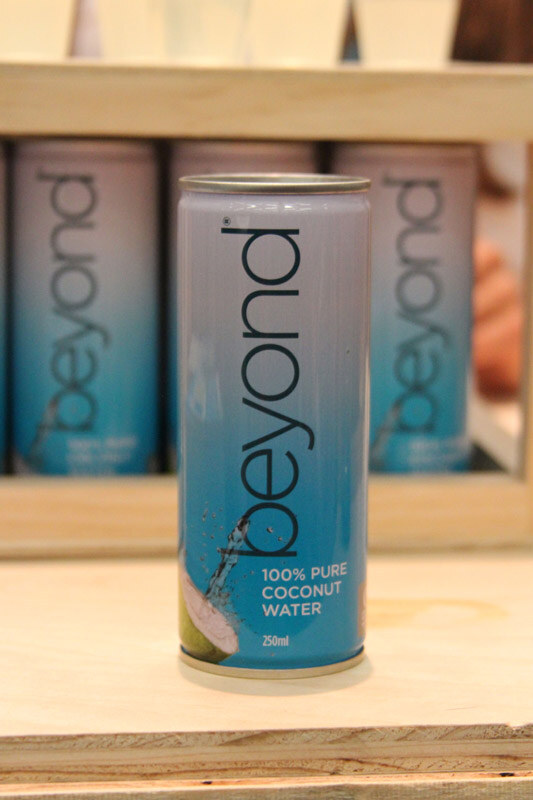 A blue 250 ml can of beyond 100% Pure Coconut Water stands on a wooden shelf in front of several more beyond cans.