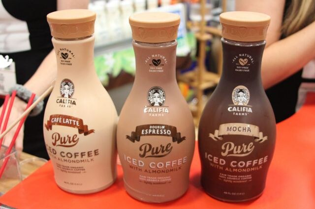Three Califia Farms Pure Iced Coffee with Almondmilk bottles in Café Latte, Double Espresso and Mocha stand on a red counter.