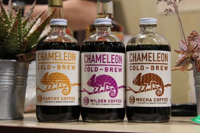 Three bottles of Chameleon Cold-Brew coffee labeled Earthy Coffee, Wilder Coffee and Mocha Coffee, beside a potted succulent.