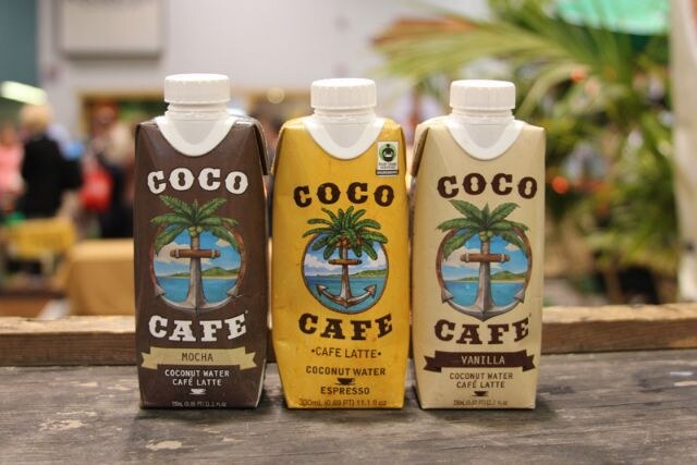 Three cartons of Coco Café coconut water coffee drink in mocha, café latte and vanilla stand side by side on a wooden surface.