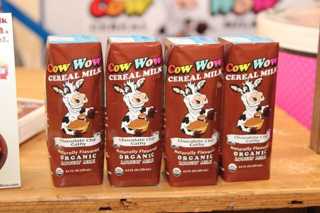 Four brown Cow Wow Cereal Milk cartons labeled Chocolate Chip Cathy, each with a cartoon cow, lined up on a wooden table.