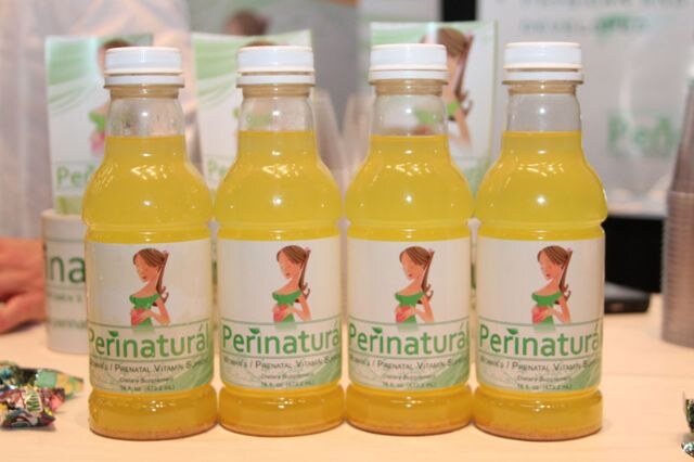 Four bottles of yellow Perinaturá prenatal vitamin drink with labels showing an illustrated pregnant woman, on a table with candy at the left.