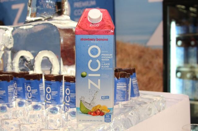 A carton of ZICO strawberry banana coconut water and juice blend sits on ice, with small blue and brown ZICO cartons around it and an ice sculpture behind.