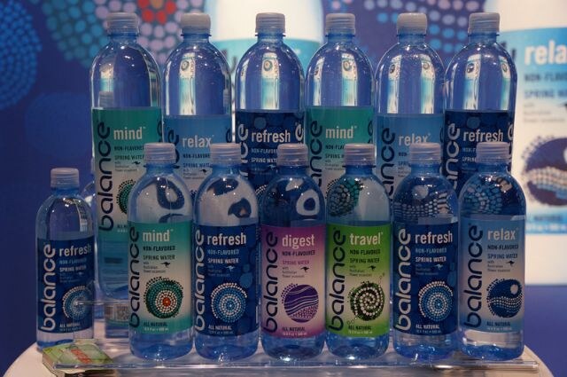 Tiered display of Balance spring water bottles labeled mind, relax, refresh, digest and travel, with dot-pattern artwork on the labels and a banner behind.