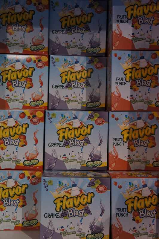 Stacked retail boxes of Flavor Blast, in grape and fruit punch varieties, filling the frame, with bottle and fruit illustrations and a red "No!" caffeine badge.