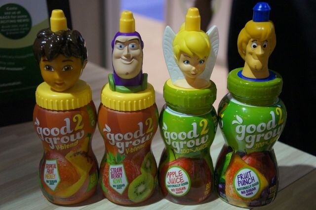 Four good2grow juice bottles with character-head tops, including a space ranger, a winged fairy and a cartoon detective, in Tropical Fruit Medley, Strawberry Kiwi, Apple Juice and Fruit Punch.