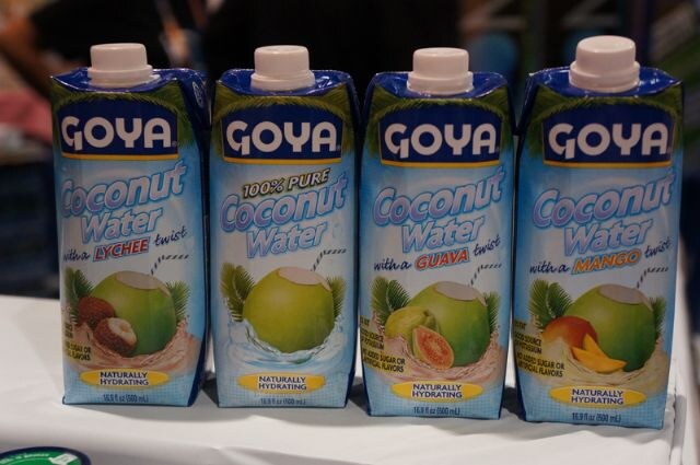 Four Goya Coconut Water cartons in a row: lychee twist, 100% pure, guava twist and mango twist, each labeled Naturally Hydrating, on a white table.