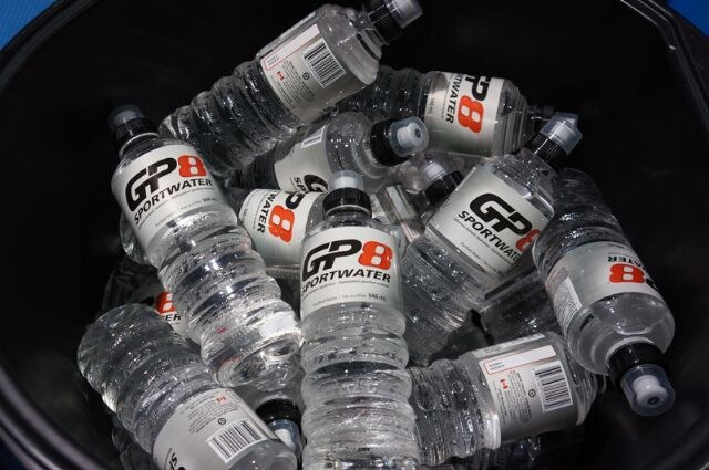 Many clear bottles of GP8 Sportwater with black caps are piled together in a dark bowl.