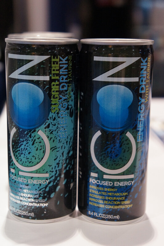 Two black and teal 8.4 fl oz cans of ION energy drink, one labeled Sugar Free and one regular with taurine, standing on a white surface.