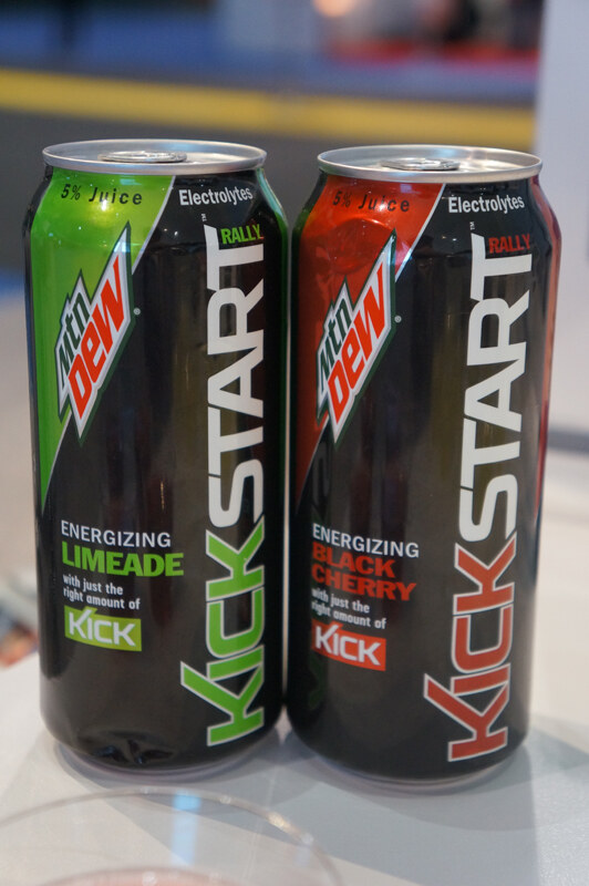 Two black cans of Mtn Dew Kickstart, one Energizing Limeade with green accents and one Energizing Black Cherry with red accents, standing side by side on a white surface.