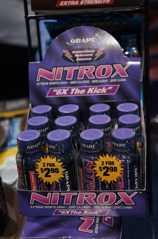 Purple retail display box of Nitrox grape extreme sports drink shots with yellow starburst labels reading 2 for $2.98.