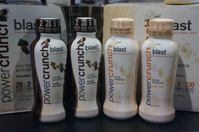 Four Power Crunch Blast protein drink bottles, two double chocolate and two vanilla cream, stand in front of their cartons.