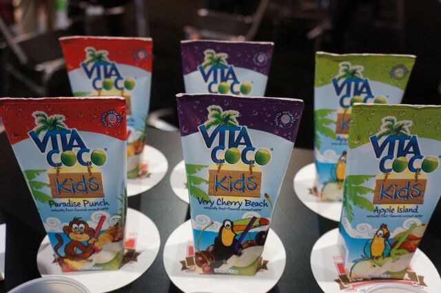 Vita Coco Kids coconut water cartons on paper coasters: Paradise Punch, Very Cherry Beach and Apple Island, with cartoon monkey, toucan and parrot illustrations.