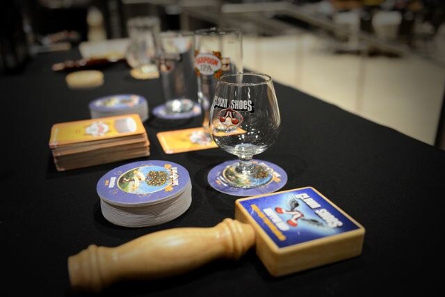 A black table holds a Harpoon IPA glass on a coaster, stacks of coasters and a wooden Cloud Shoes tap handle with a blue label.