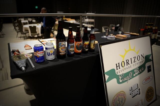 A table displays beer bottles and cans, including Harpoon IPA and UFO White, beside a Horizon Beverage Company Craft Beer sign listing Cloud Shoes among its logos.