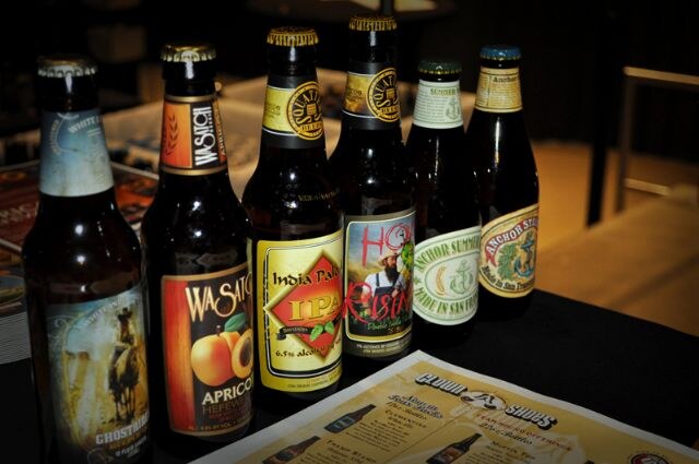 Six beer bottles stand in a row on a table, including Wasatch Apricot Hefeweizen and Anchor Summer, with a Cloud Shoes menu sheet in front.