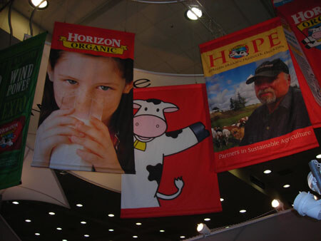Hanging banners overhead show a child drinking milk for Horizon Organic, a cartoon cow, and a bearded man in a cap on a Hope banner reading Partners in Sustainable Agriculture.