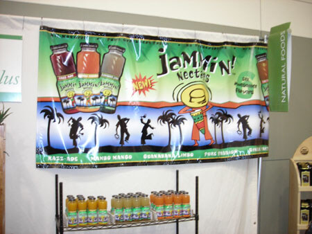 A large Jammin' Nectars banner with palm trees and dancing silhouettes hangs above a wire rack of bottled nectars in green, orange and other colors. A green Natural Foods sign is at right.