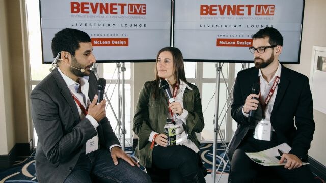 Three people with microphones sit and talk in the BevNET Live Livestream Lounge. Screens behind them read sponsored by McLean Design, and the woman in the middle holds a bottle.